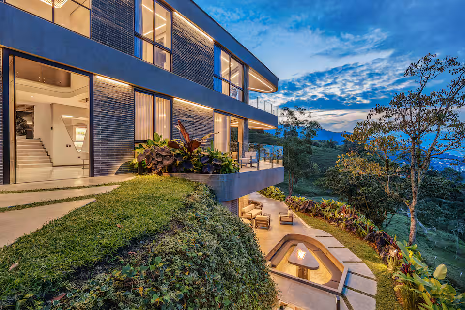 Exterior view of the Medellin retreat villa lit at dusk with balconies, gardens, and hillside views